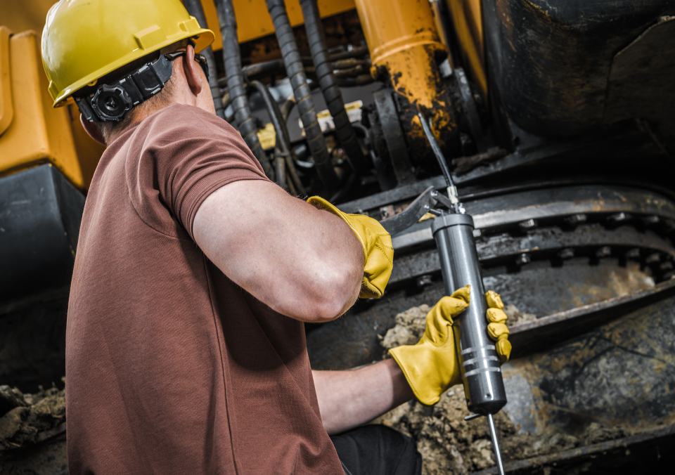 Worker greasing machinery with a lubrication gun.